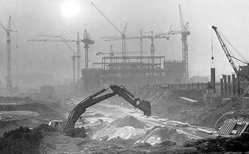 Die Baustelle des Universitätshauptgebäudes im Jahr 1972. Im Vordergrund gräbt ein Bagger in der Erde. Im Hintergrund ist der beginnende Rohbau des Hauptgebäudes mit zahlreichen Kränen zu sehen.