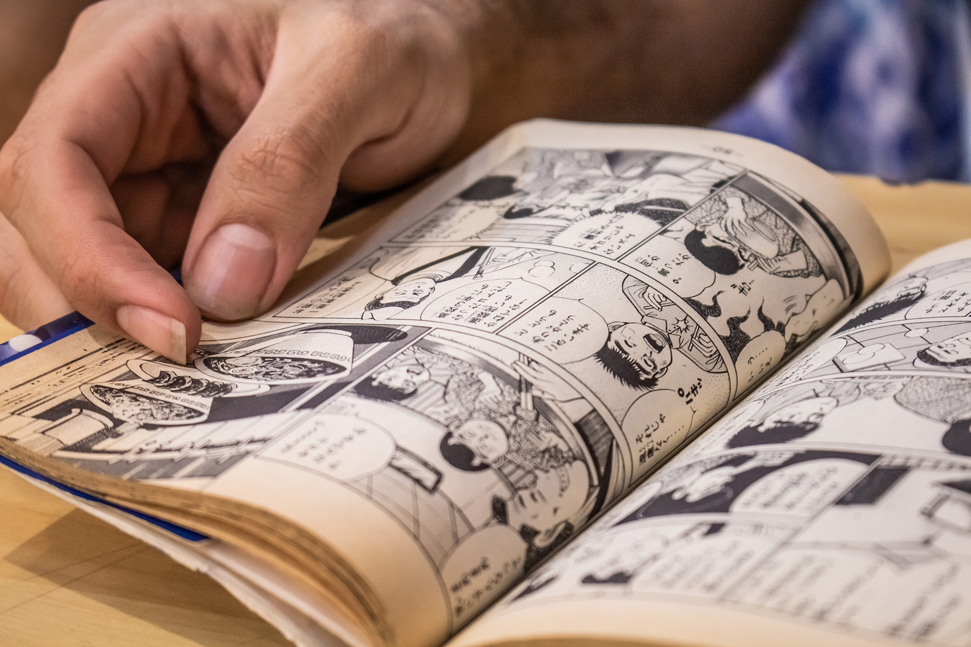 A graphic novel lies on a table, held in one hand
