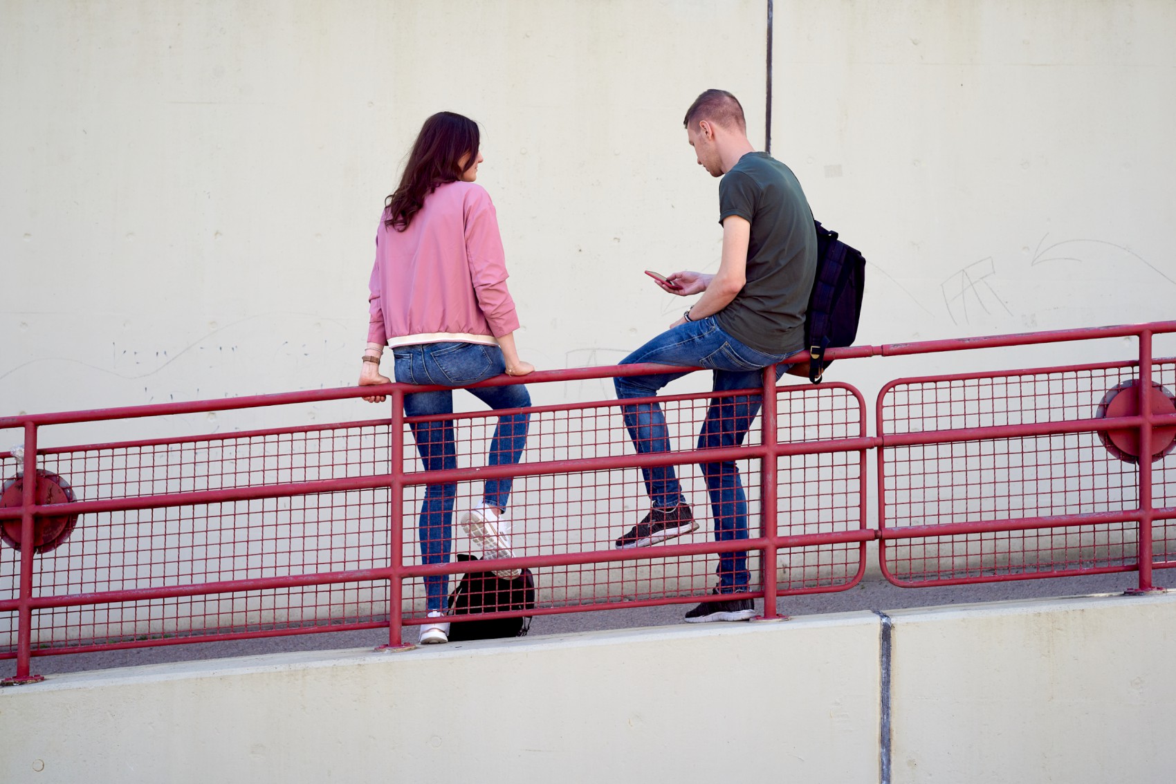 Zwei Studierende sitzen auf dem roten Geländer an der Rampe