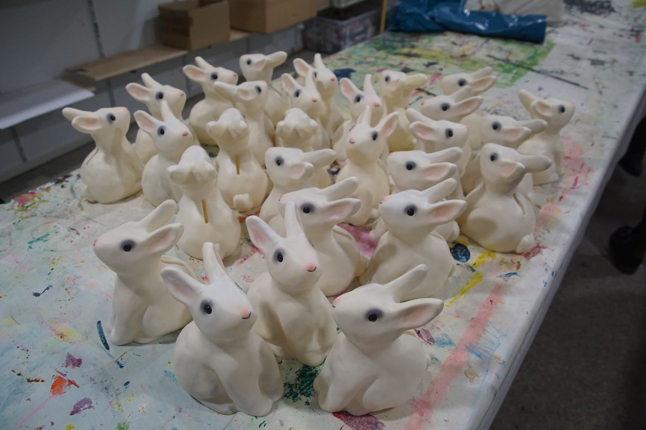 Viele weiße Plastik-Hasen auf einem bunten Tisch.