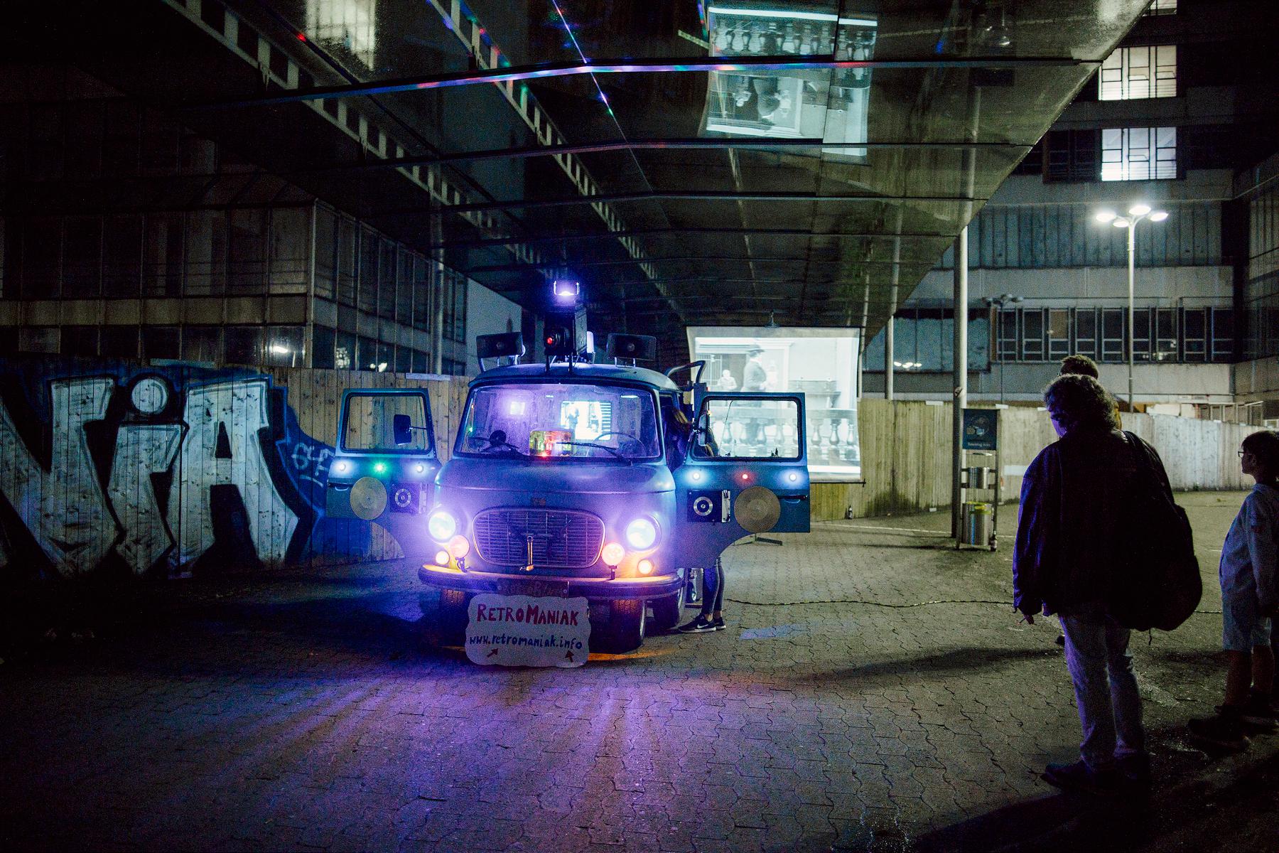 Foto von der Nacht der Klänge 2019 nach Einbruch der Dunkelheit: Beleuchteter blauer Oldtimer-Bus als Klanginstallation vor dem Universitätshauptgebäude.